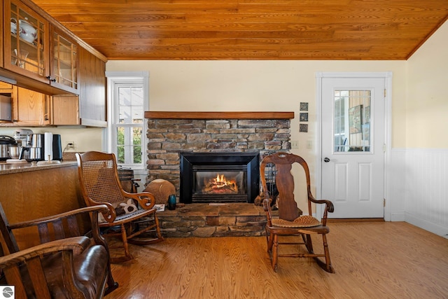 sitting room with a stone fireplace, light hardwood / wood-style flooring, and wood ceiling