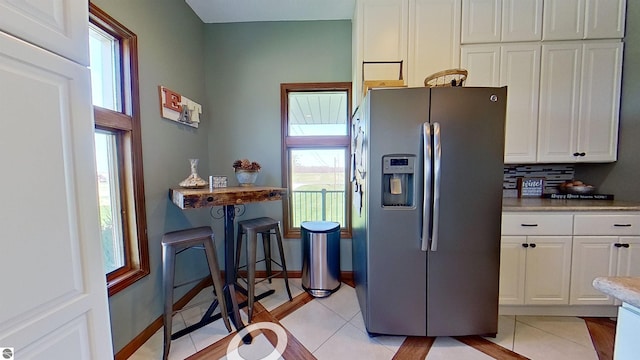 kitchen featuring stainless steel refrigerator with ice dispenser, light tile patterned floors, white cabinetry, and a healthy amount of sunlight