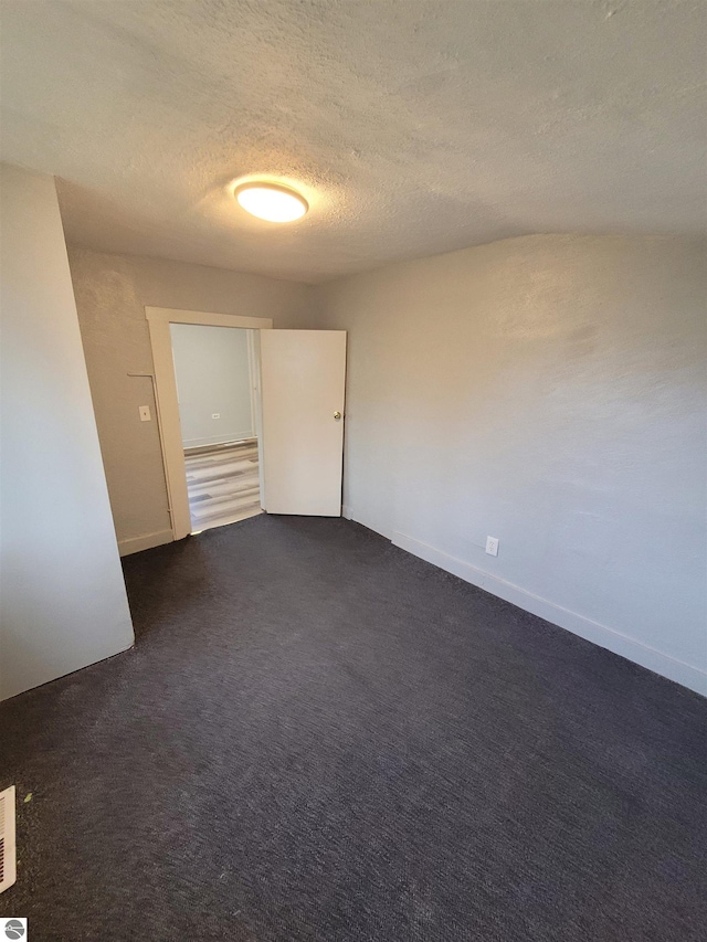 empty room featuring a textured ceiling and dark carpet