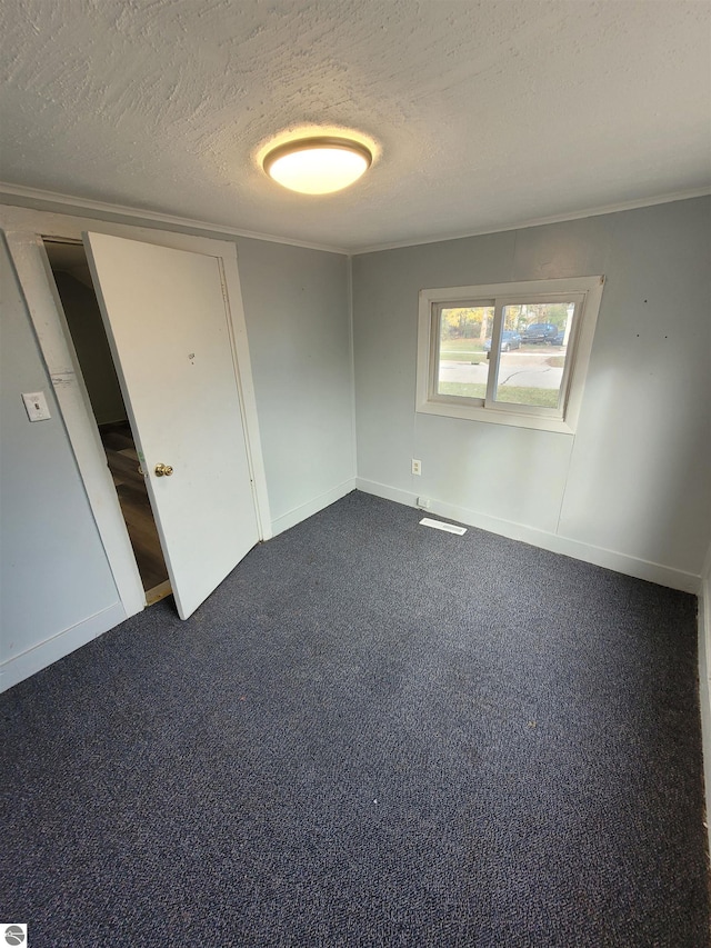 spare room featuring dark carpet and a textured ceiling