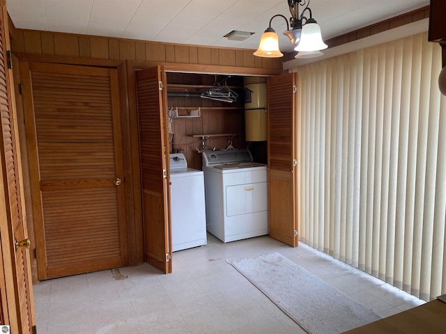 clothes washing area featuring washing machine and dryer, wooden walls, and a notable chandelier