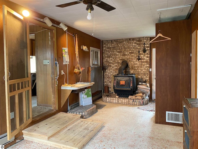 interior space with ceiling fan, a wood stove, and wooden walls