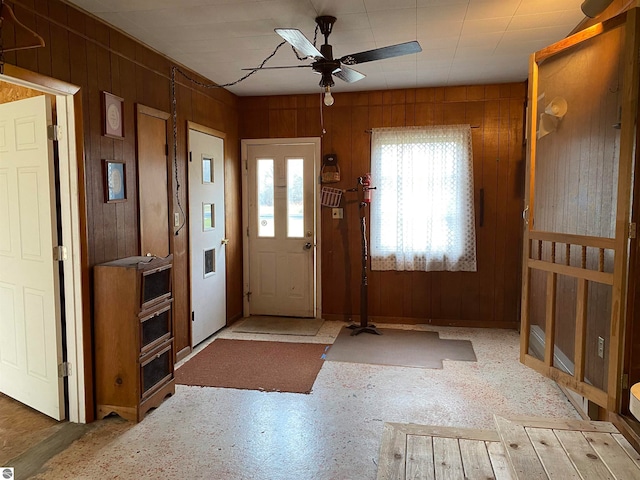 foyer with ceiling fan and wooden walls