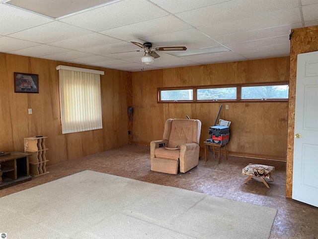 living area with wooden walls, a drop ceiling, and ceiling fan