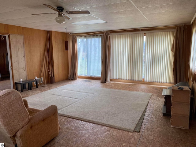 sitting room featuring ceiling fan, a drop ceiling, and wooden walls