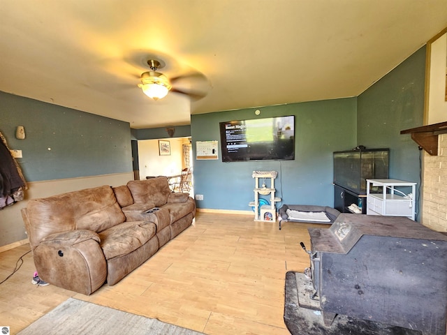 living area with baseboards, a wood stove, wood finished floors, and a ceiling fan