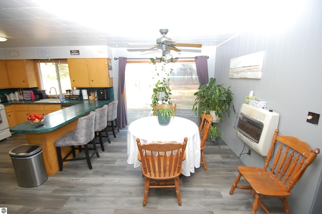 dining area with ceiling fan, light wood-type flooring, sink, and heating unit