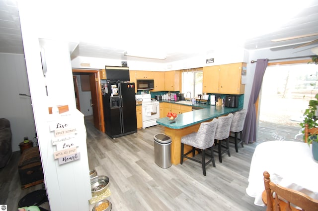 kitchen featuring black appliances, sink, light hardwood / wood-style flooring, a kitchen bar, and kitchen peninsula