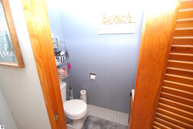 bathroom with tile patterned flooring, toilet, and wooden walls