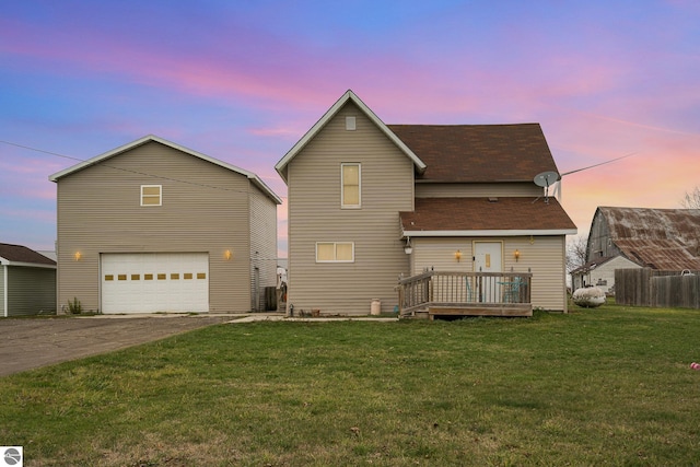 back house at dusk featuring a wooden deck, a yard, and a garage