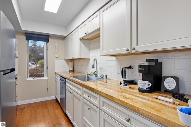 kitchen with sink, wood counters, light hardwood / wood-style floors, white cabinets, and appliances with stainless steel finishes