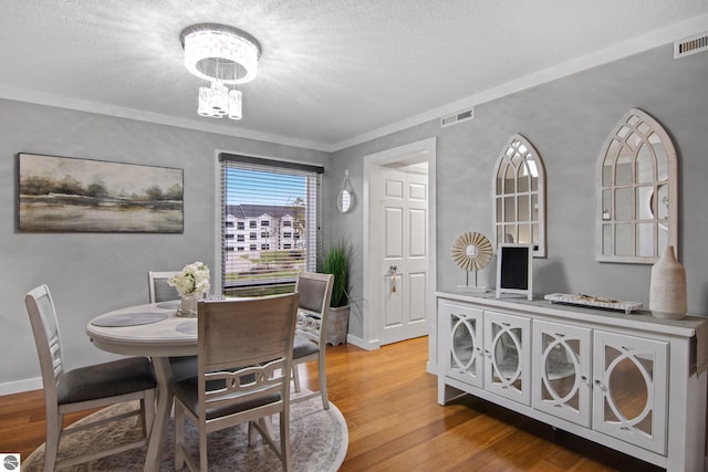 dining room with hardwood / wood-style floors, ornamental molding, a textured ceiling, and an inviting chandelier