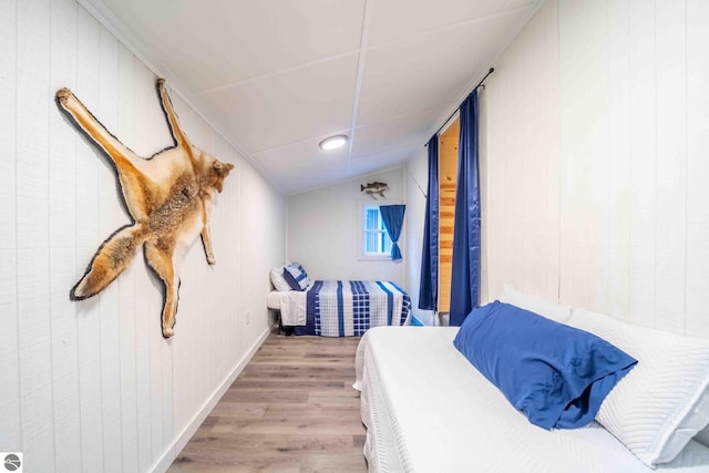 bedroom with vaulted ceiling, light hardwood / wood-style flooring, and wood walls