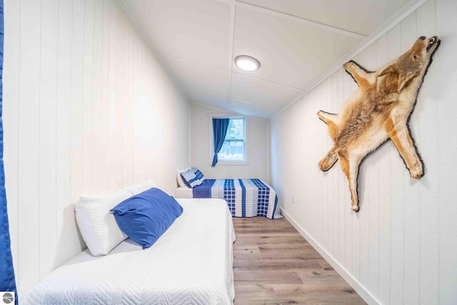 bedroom with wood walls, crown molding, light hardwood / wood-style floors, and vaulted ceiling