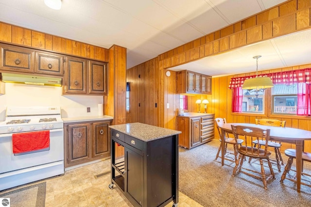 kitchen featuring a center island, hanging light fixtures, light carpet, wooden walls, and white stove