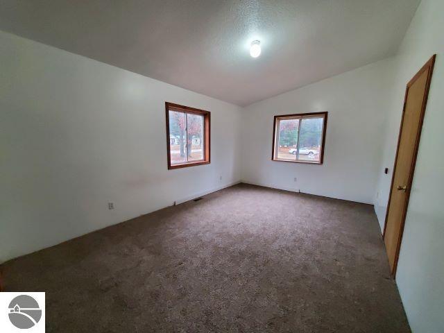 spare room featuring dark colored carpet and lofted ceiling