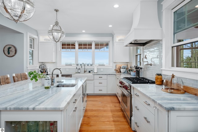 kitchen with a center island with sink, custom exhaust hood, decorative backsplash, and stainless steel range