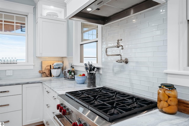 kitchen with high end range, white cabinetry, plenty of natural light, and custom exhaust hood