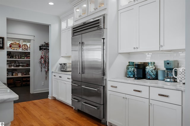 kitchen with white cabinetry, built in fridge, light stone countertops, and light wood-type flooring