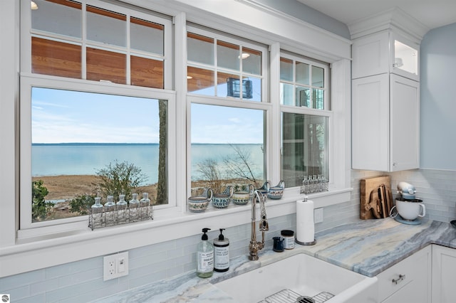 interior details with white cabinets, a water view, and tasteful backsplash