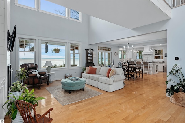 living room with a notable chandelier, light wood-type flooring, and a towering ceiling