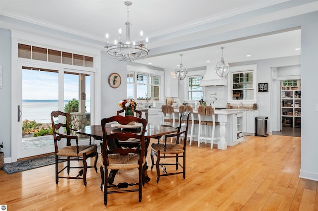 dining space featuring an inviting chandelier, a water view, crown molding, and light hardwood / wood-style flooring