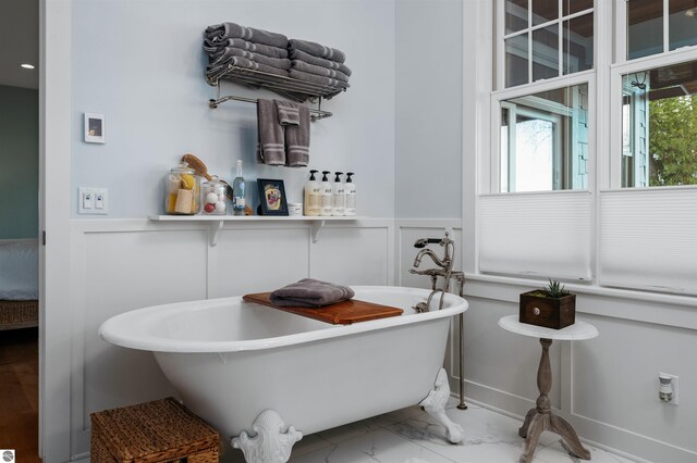 91 S Nanagosa Trl, Suttons Bay, MI 49682 - bathroom with a freestanding tub, a wainscoted wall, marble look tile flooring, and a decorative wall