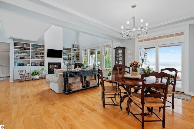 91 S Nanagosa Trl, Suttons Bay, MI 49682 - dining space with a chandelier, a glass covered fireplace, light wood-style floors, crown molding, and built in features