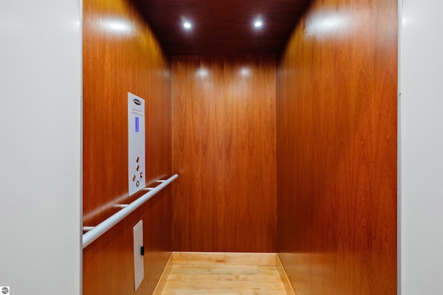 details with elevator, wood walls, and hardwood / wood-style floors