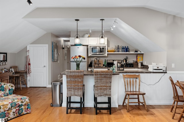 kitchen featuring kitchen peninsula, appliances with stainless steel finishes, a kitchen breakfast bar, white cabinets, and hanging light fixtures