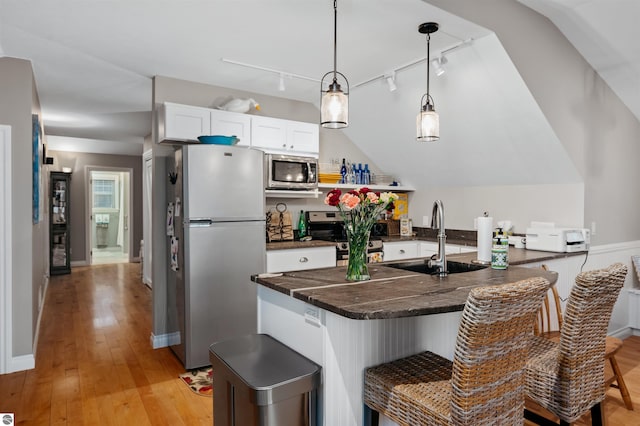 kitchen featuring pendant lighting, white cabinets, rail lighting, appliances with stainless steel finishes, and light hardwood / wood-style floors