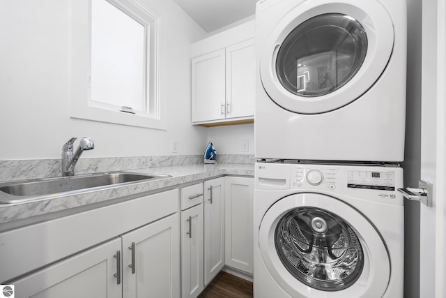 washroom with cabinets, stacked washer / dryer, and sink