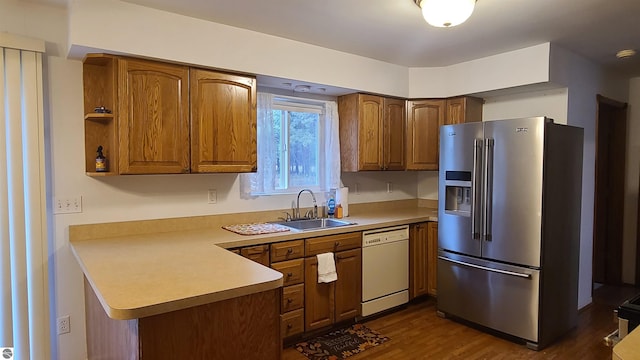 kitchen with kitchen peninsula, stainless steel fridge, white dishwasher, dark wood-type flooring, and sink