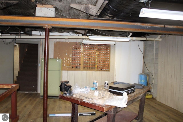 basement with wood-type flooring, white refrigerator, and wooden walls