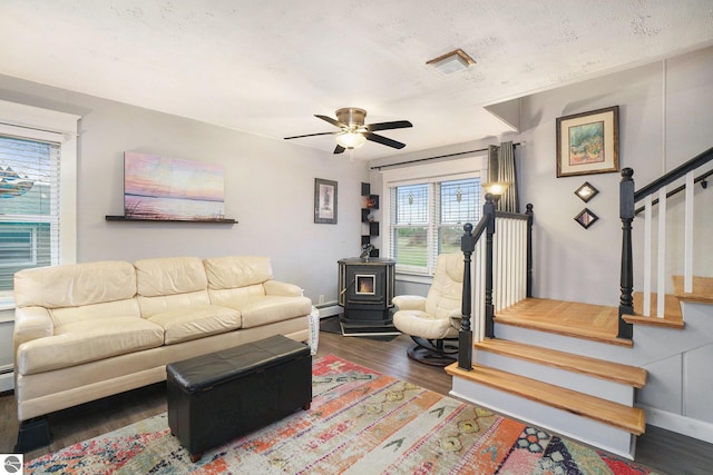 living room with a textured ceiling, ceiling fan, a baseboard heating unit, dark hardwood / wood-style floors, and a wood stove