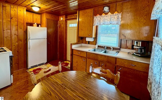 kitchen featuring white appliances, sink, wooden walls, light hardwood / wood-style floors, and wood ceiling