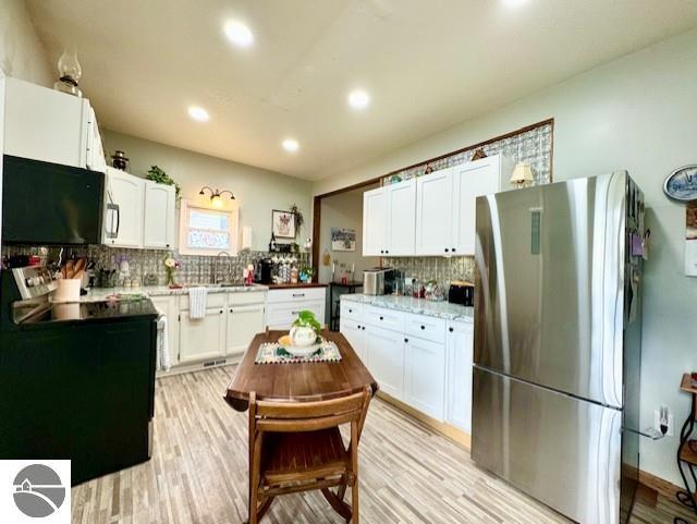 kitchen with white cabinets, stainless steel fridge, light hardwood / wood-style flooring, and tasteful backsplash