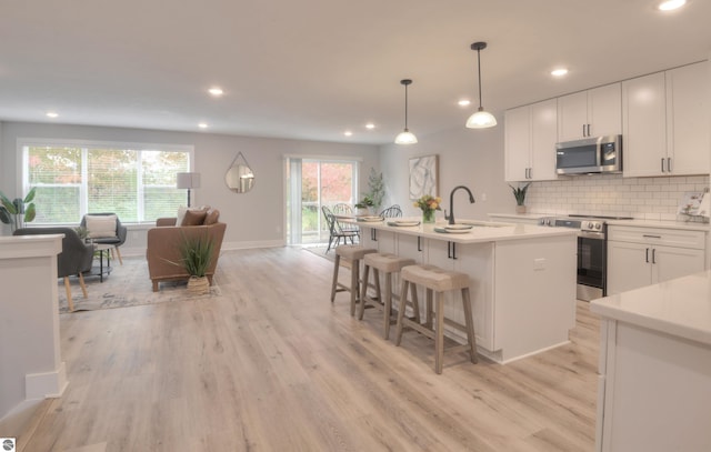 kitchen with white cabinetry, sink, a healthy amount of sunlight, stainless steel appliances, and a center island with sink