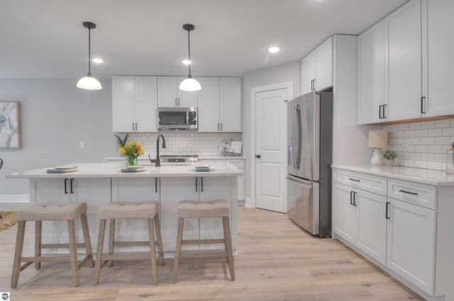 kitchen featuring white cabinetry, stainless steel appliances, tasteful backsplash, pendant lighting, and light wood-type flooring