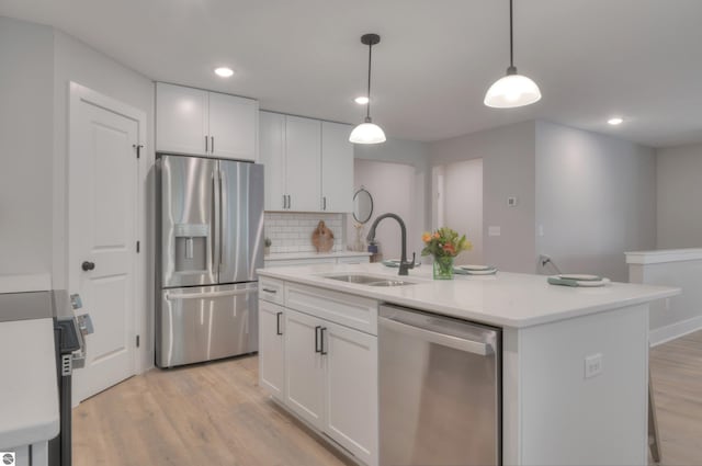 kitchen featuring light wood-type flooring, stainless steel appliances, white cabinetry, and a kitchen island with sink