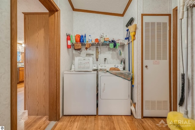 clothes washing area featuring washing machine and dryer, light hardwood / wood-style floors, and ornamental molding