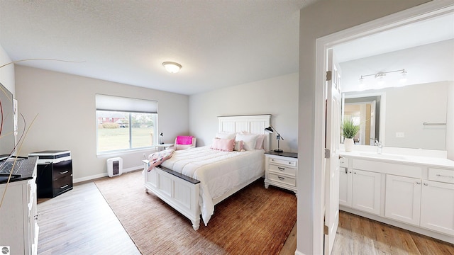 bedroom with a textured ceiling, ensuite bathroom, and light hardwood / wood-style flooring