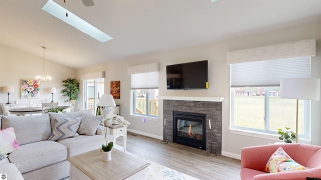 living room featuring vaulted ceiling with skylight, plenty of natural light, light wood-type flooring, and a fireplace