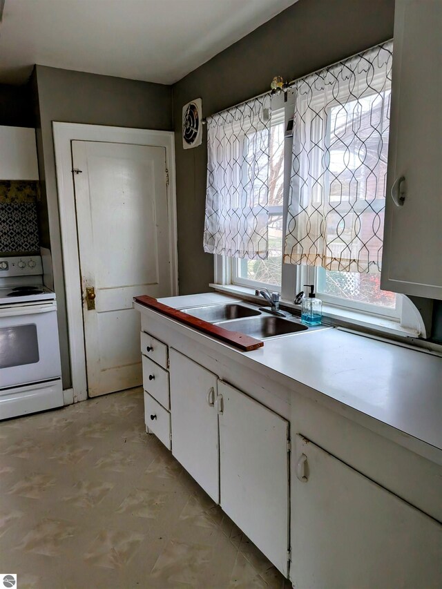 kitchen with electric range, white cabinetry, and sink