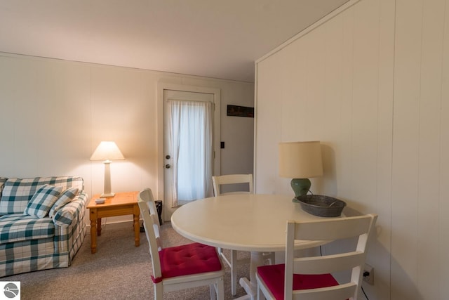 carpeted dining space featuring wood walls