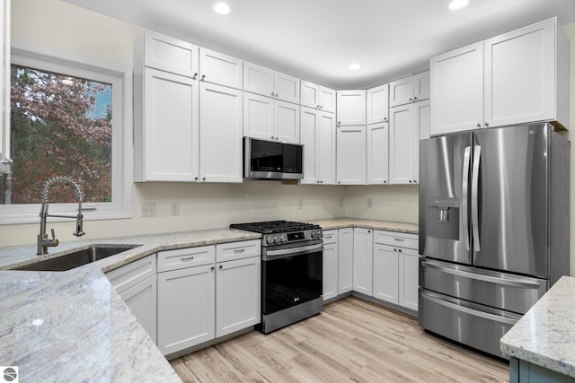 kitchen with white cabinets, sink, light stone countertops, and stainless steel appliances