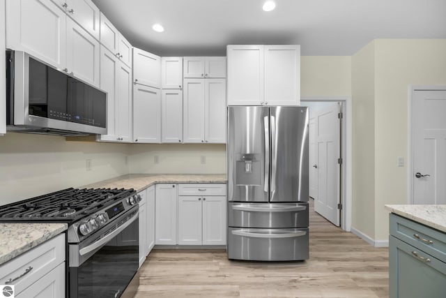 kitchen featuring white cabinets, light stone countertops, light wood-type flooring, and appliances with stainless steel finishes