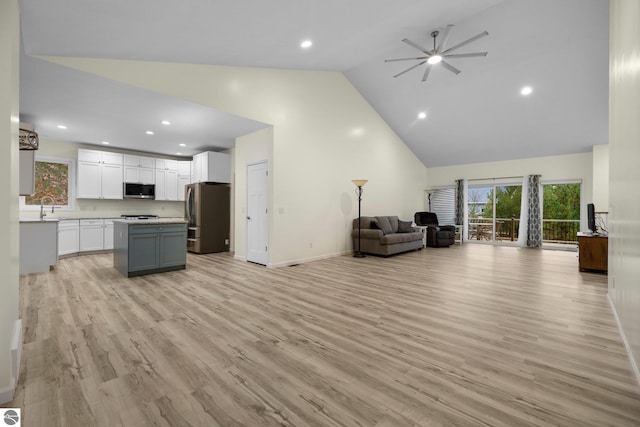 unfurnished living room with ceiling fan, light wood-type flooring, sink, and high vaulted ceiling