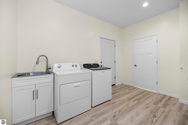 laundry area featuring washer and clothes dryer, sink, cabinets, and light wood-type flooring