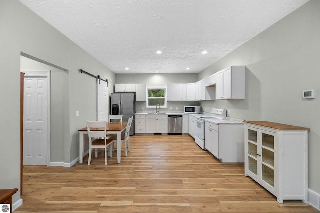 kitchen with sink, light hardwood / wood-style flooring, a barn door, appliances with stainless steel finishes, and white cabinetry